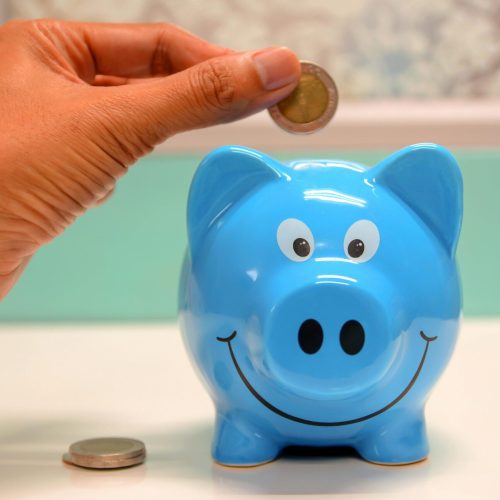 Hand inserting a coin into a blue piggy bank for savings and money management.
